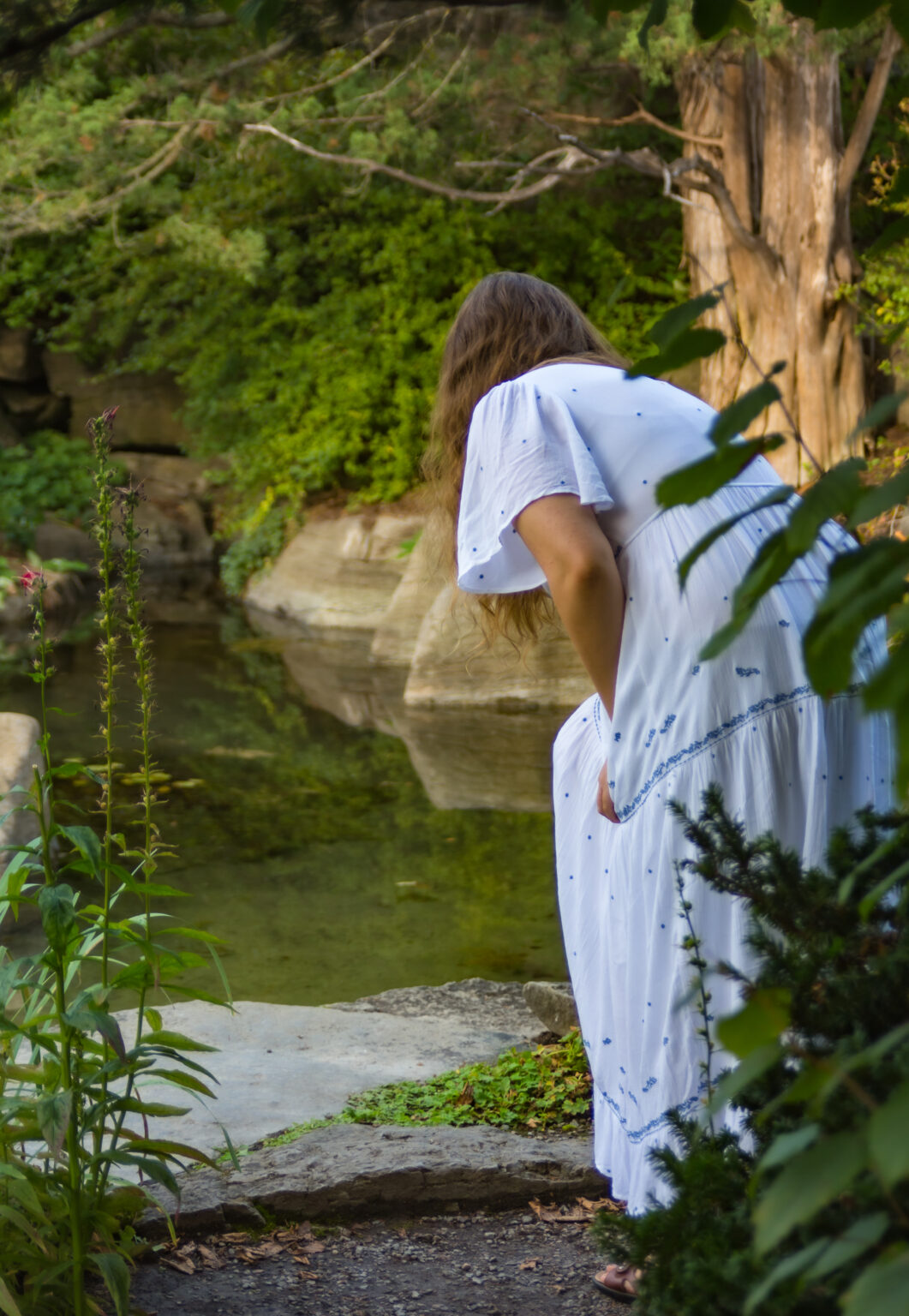 Femme en robe blanche près d'un étang.